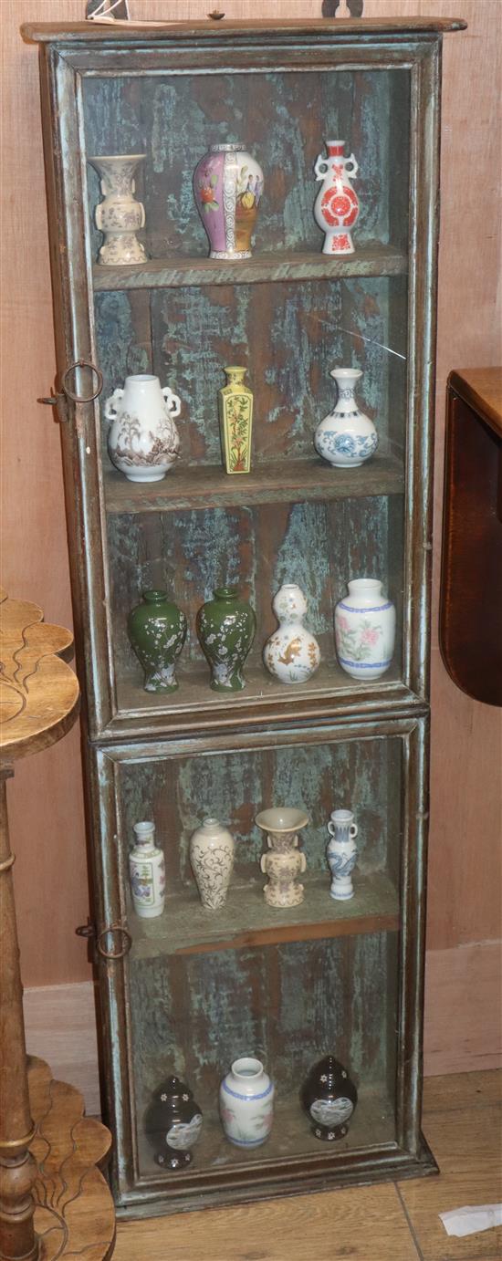 A distressed hardwood two door glazed wall mounted cabinet, together with a collection of 17 miniature vases after early Chinese origin